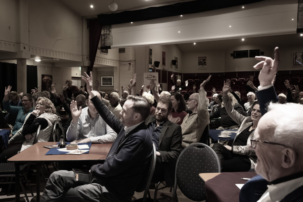 Het publiek steekt de hand op.